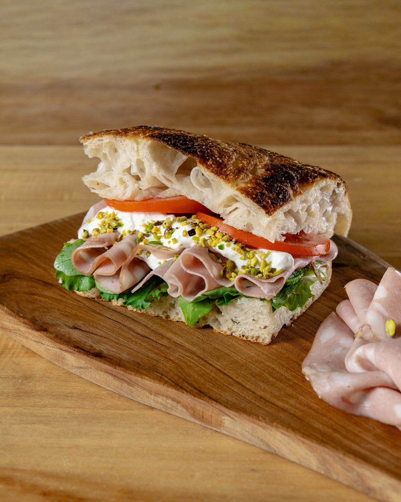 Detaliu cu interiorul unui panino Francesca: mortadella cu fistic, brânză cremoasă, roșii și salată verde