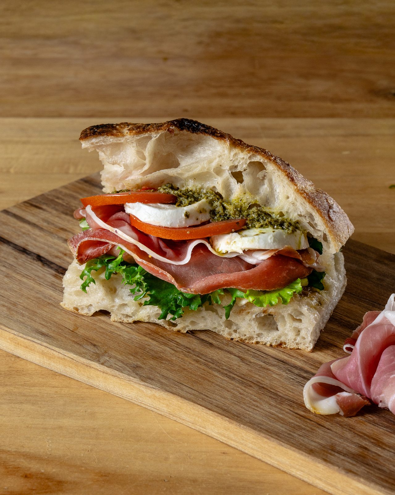 Detaliu cu straturile unui panino cu prosciutto, mozzarella di bufala, pesto și roșii